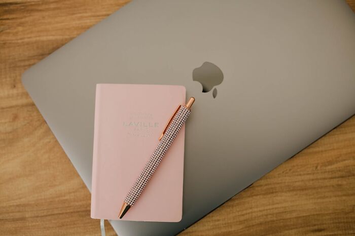 Closed silver laptop on wooden table with pink notebook and rose gold pen, representing iconic satisfying situations.