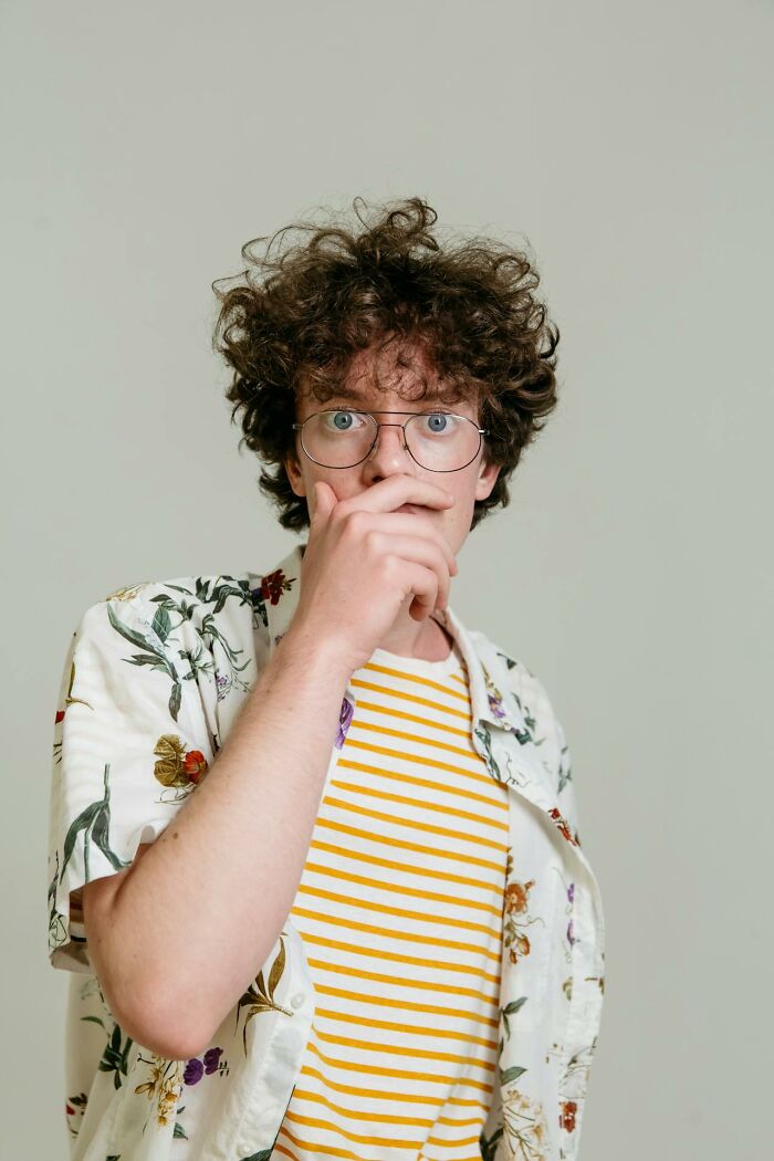 Young man with curly hair and glasses looking shocked, illustrating unexplainable medical events and bad prognosis miracles.