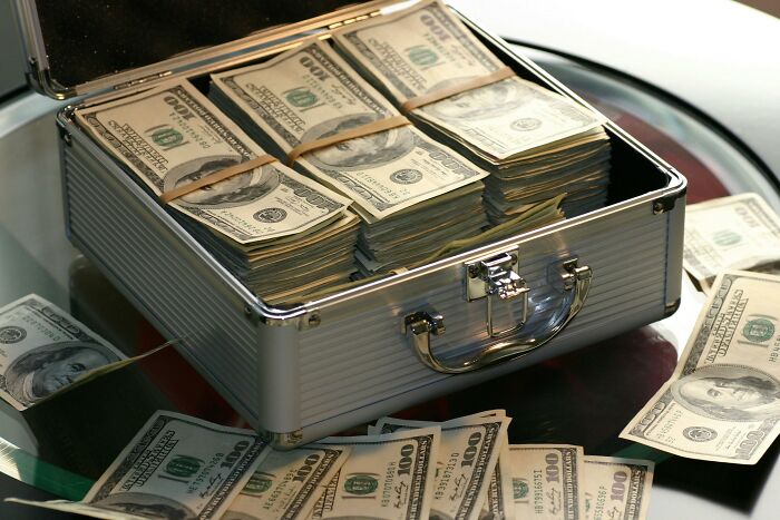Open metal briefcase filled with stacks of hundred-dollar bills, symbolizing wealth and rich people’s opinions.