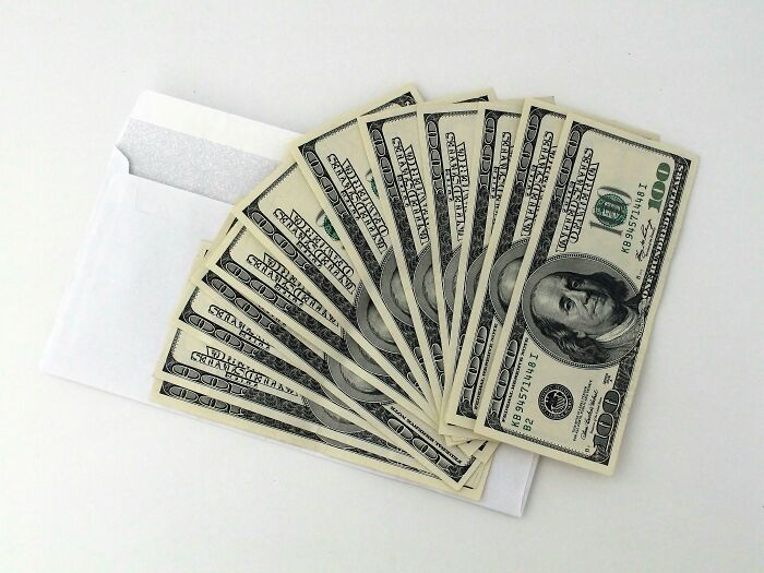 Fan of hundred-dollar bills fanned out atop a white envelope representing wealth and financial discussions.