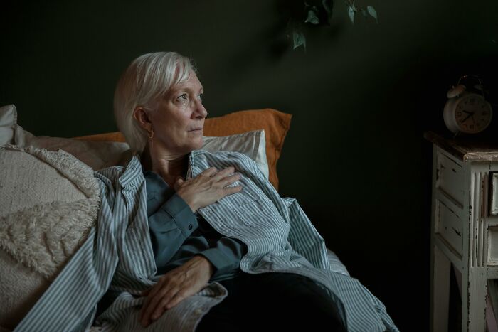 Elderly woman looking reflective while resting on a bed, evoking thoughts of family secrets and personal stories.
