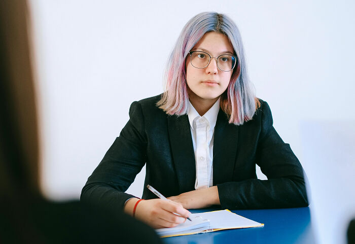 Young woman with glasses and pink hair taking notes, illustrating weird and satisfying situations where people said not my problem anymore.