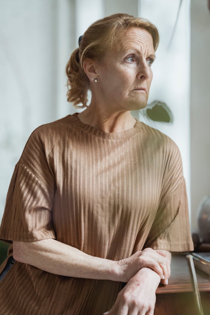 Woman looking out a window with a serious expression, reflecting after snapping at her controlling vegan friend.