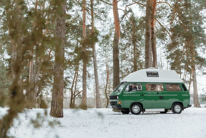 Green camper van parked in a snowy forest, illustrating solitude from worst coworkers making work feel like a nightmare.