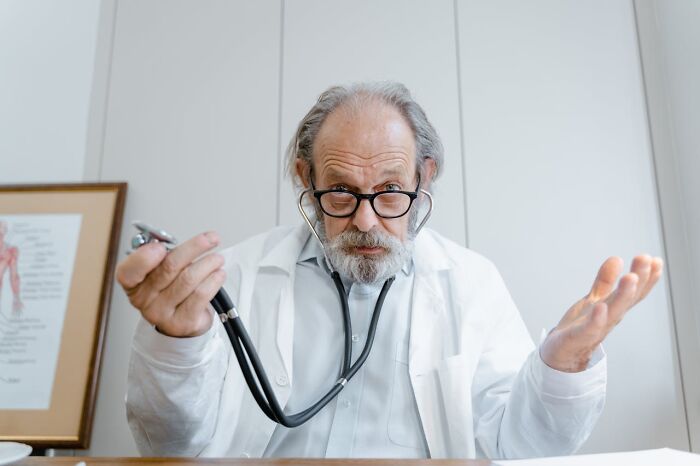 Elderly male doctor with glasses and white coat holding a stethoscope, symbolizing unexplainable medical events and prognosis.