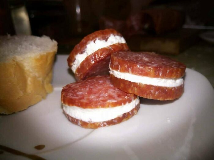 Funny Eastern European snack with salami slices filled with cream cheese on a white plate next to bread.