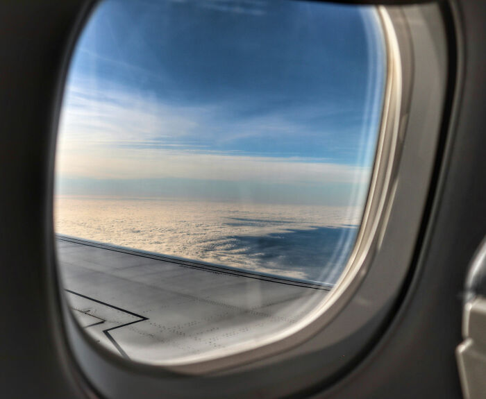 Airplane window view of wing and clouds, passenger highlights sardine can seating and cramped legroom Airplane window view of wing and clouds, passenger highlights sardine can seating and cramped legroom