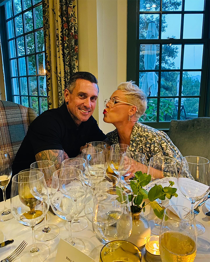 Pink and a companion seated at a table with multiple wine glasses, sharing a joyful moment indoors. Pink and a companion seated at a table with multiple wine glasses, sharing a joyful moment indoors.