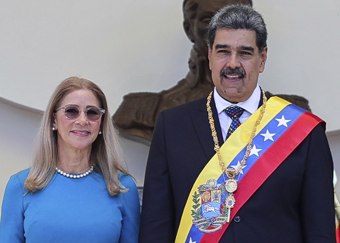 Venezuelan leader wearing presidential sash standing next to a woman in blue, related to Pentagon pizza spike theory during attack. Venezuelan leader wearing presidential sash standing next to a woman in blue, related to Pentagon pizza spike theory during attack.