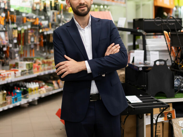 Man in navy suit standing with arms crossed in a store aisle, illustrating coworker stories about unhinged behavior at work.