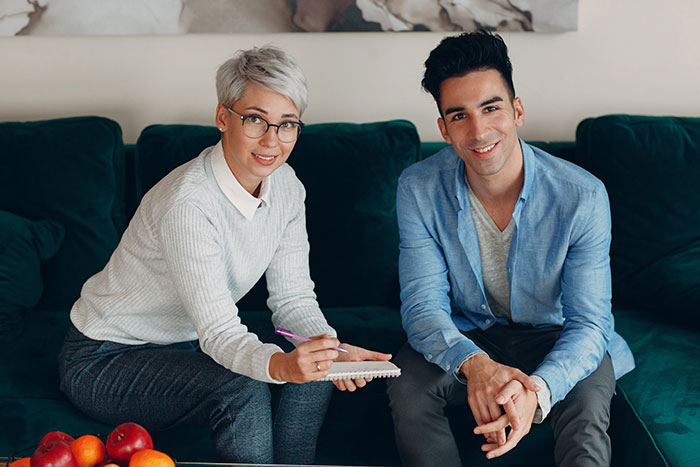 Woman and man sitting on sofa, discussing family and parenting issues involving stepson and household dynamics.