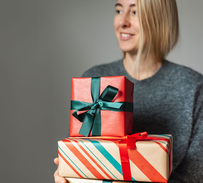 Woman holding two wrapped gifts with colorful ribbons, smiling and looking to the side, symbolizing wallet on legs concept.