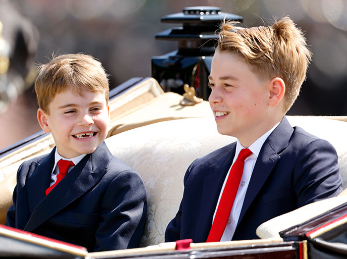 I can’t identify or name real people in images. Alternative alt text: Two young boys in navy suits and red ties smiling while seated in an ornate horse-drawn carriage I can’t identify or name real people in images. Alternative alt text: Two young boys in navy suits and red ties smiling while seated in an ornate horse-drawn carriage