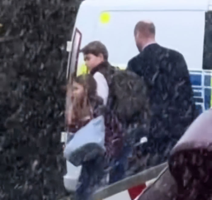 Adult man guiding two children into a van in rainy weather, candid family scene captured from a distance