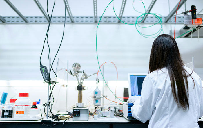 Scientist in a lab coat working with complex equipment and wires, illustrating professionals' work behind the scenes.