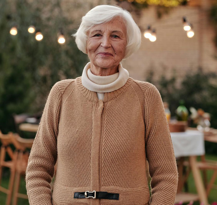 Elderly woman in a beige sweater smiling outdoors, symbolizing MIL who played the long game with furniture rearrangement.