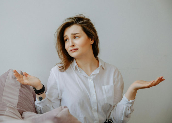 Young woman in white shirt shrugging with a puzzled expression, illustrating MIL thinks she&rsquo;s won against DIL conflict.