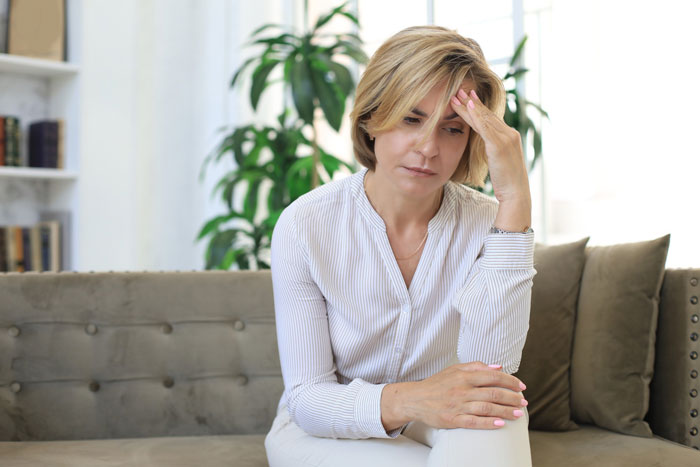 Worried mom sitting on couch, clinging to daughter's wedding dress after family conflict over dress possession.