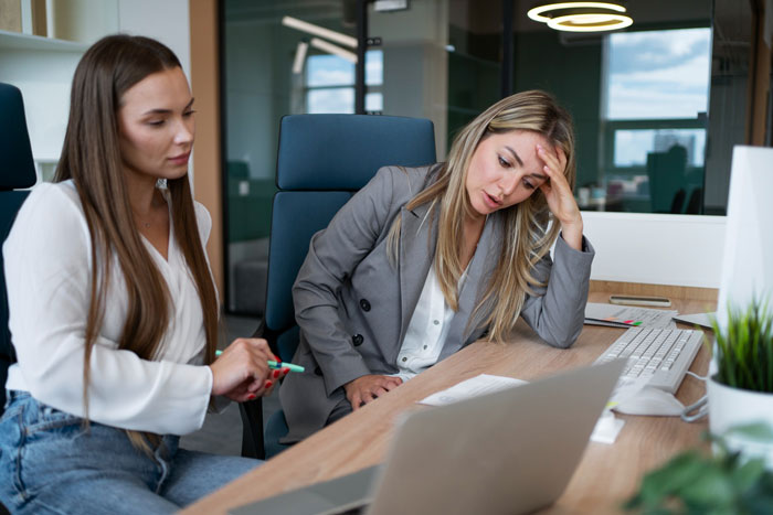 Two women in an office discussing a work issue, one looking stressed, highlighting refuse shaving legs work concerns. Two women in an office discussing a work issue, one looking stressed, highlighting refuse shaving legs work concerns.