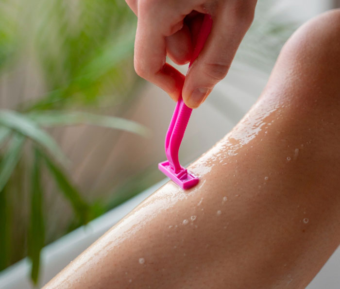 Hand holding pink razor shaving wet leg emphasizing the topic of refuse shaving legs work and personal care choices. Hand holding pink razor shaving wet leg emphasizing the topic of refuse shaving legs work and personal care choices.