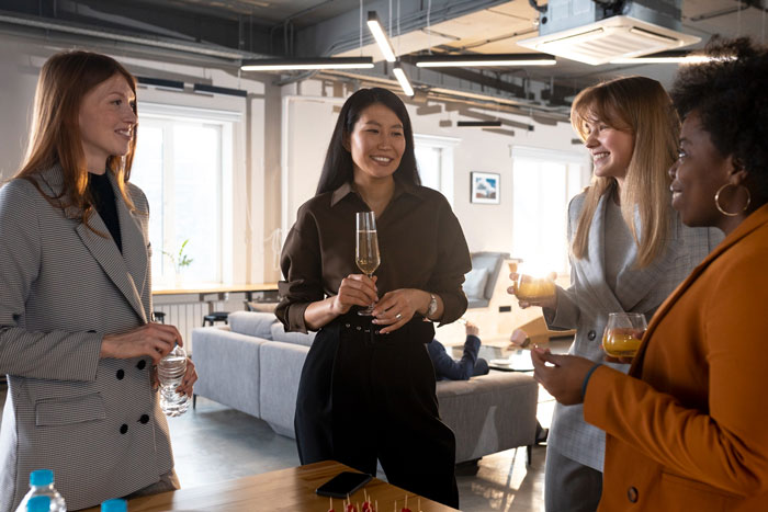 Four women enjoying drinks at a casual happy hour gathering, socializing and laughing in a modern living room.