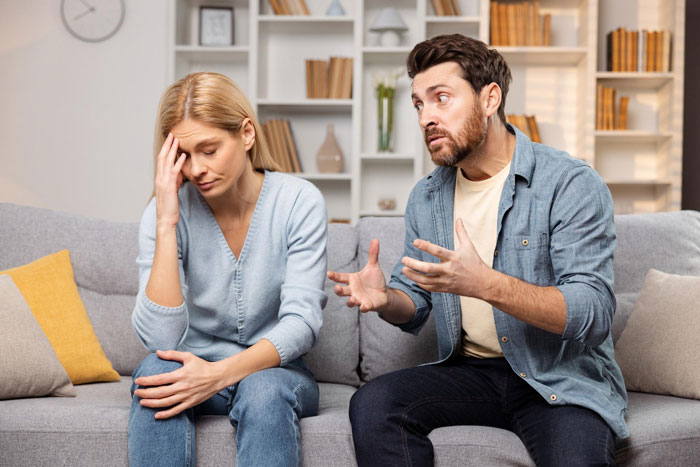 Couple arguing on a couch as husband talks angrily and pregnant wife looks upset and distant in a home setting