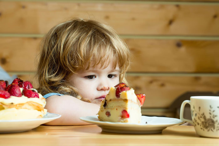 Little girl refusing to eat a slice of strawberry cake, showing reluctance and hesitation at the table. Little girl refusing to eat a slice of strawberry cake, showing reluctance and hesitation at the table.