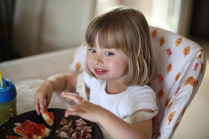Little niece eating food happily in high chair while someone is refusing to give food to her.