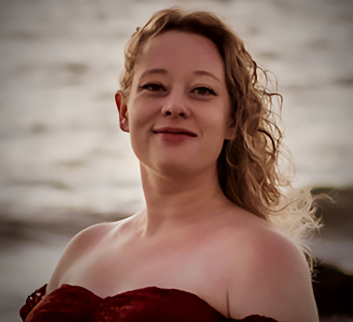 Young woman with curly hair standing near the ocean, related to father of ICE agent and immigrant wife story.