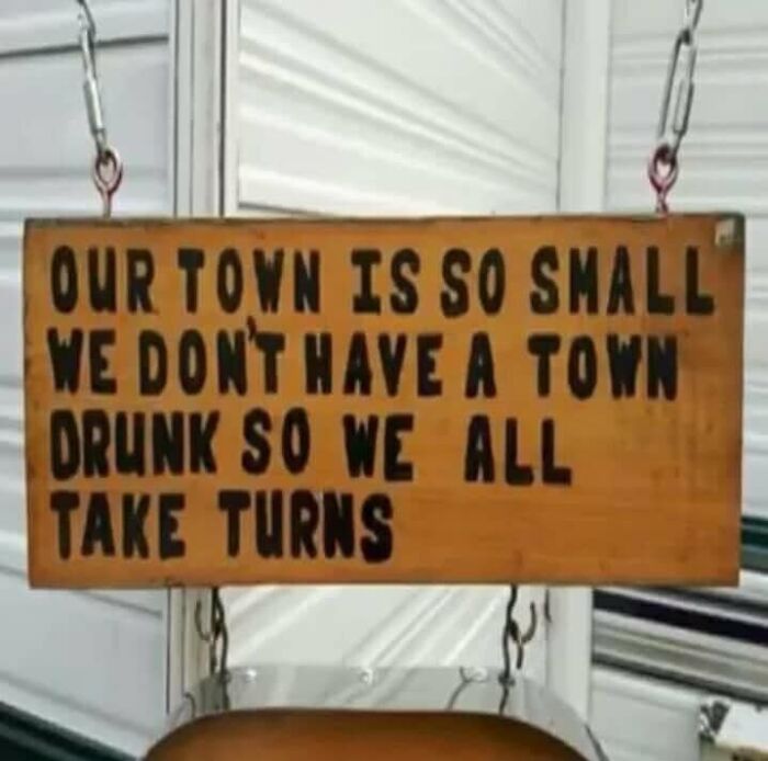 Wooden sign humorously stating a small town has no town drunk because everyone takes turns, relatable to restaurant workers.