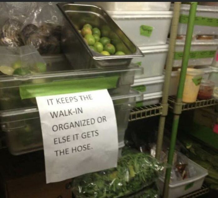 Storage area in a restaurant walk-in cooler with a humorous sign about keeping it organized for restaurant workers.