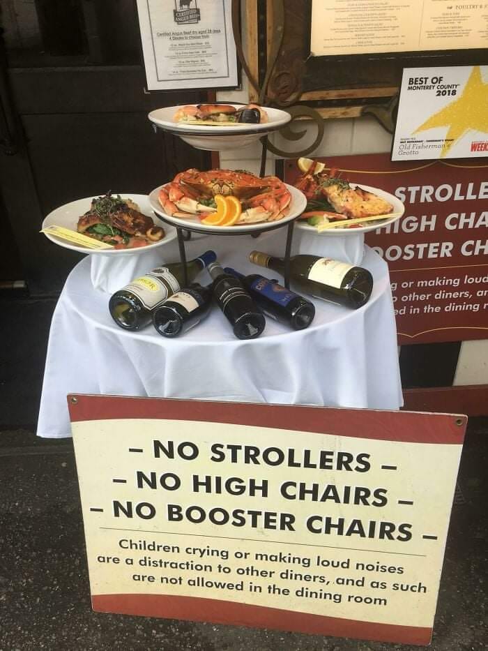 Restaurant display with seafood plates, wine bottles, and a sign about no strollers, high chairs, or booster chairs.