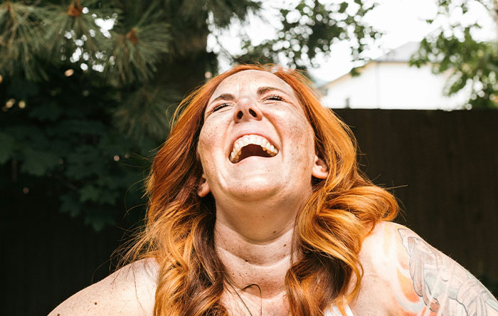 Red-haired woman laughing joyfully outdoors, capturing the moment of people getting the last laugh with glorious revenge.
