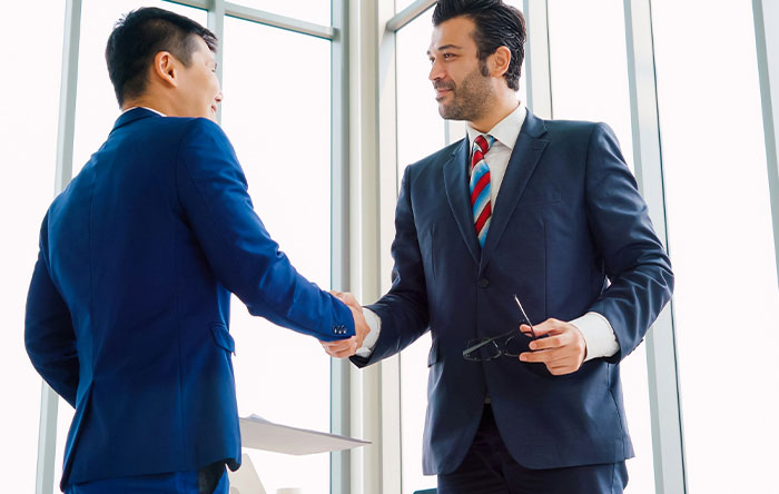 Two businessmen in suits shaking hands in a bright office, symbolizing success and glorious revenge moments.