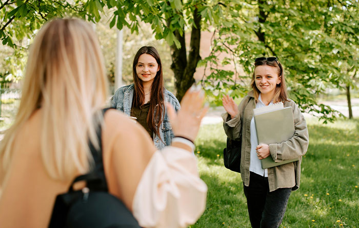 Three young women outdoors smiling and waving, capturing a moment of people getting the last laugh with glorious revenge.