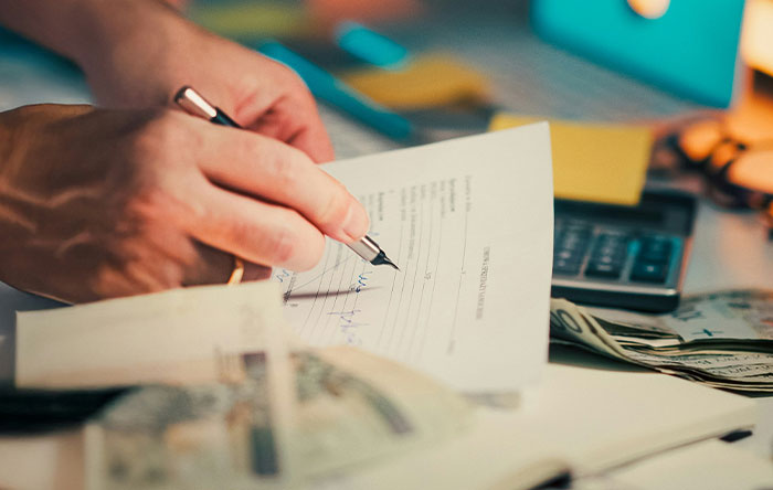 Close-up of a hand signing a document with cash and a calculator nearby, illustrating people getting the last laugh through revenge.