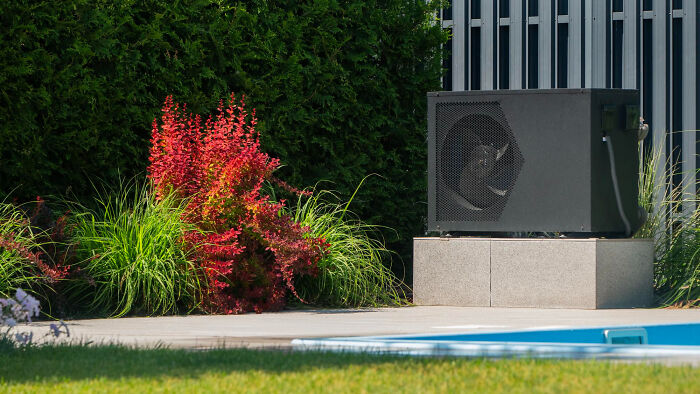 Outdoor poolside with lush greenery and a modern air conditioning unit showcasing rich people lifestyle norms.