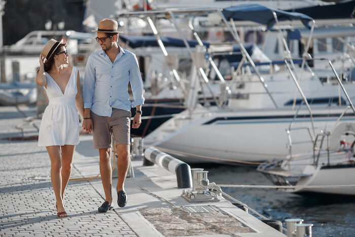 Couple dressed stylishly walking hand in hand by luxury yachts, illustrating rich people norms and wealthy lifestyle.