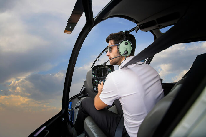Man wearing headset piloting a helicopter at sunset, illustrating rich people norms of the 1 percent lifestyle.