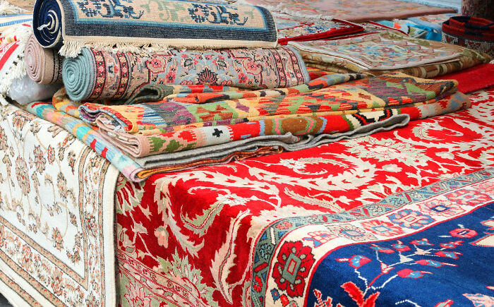 Stack of colorful rich people luxury rugs with intricate patterns, showcasing norms of the 1 percent’s high-end lifestyle.
