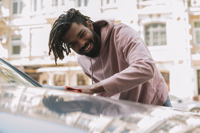Man with dreadlocks cleaning a luxury car, illustrating unique rich people norms shared by insiders on the 1 percent.