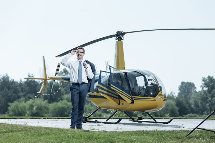 Wealthy man in business attire standing by a yellow helicopter, illustrating rich people norms and lifestyle insights.