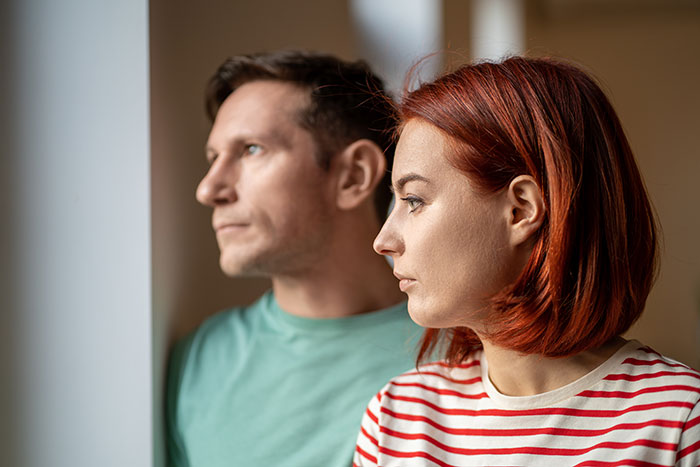 Woman with red hair and man in green shirt looking thoughtfully out window, reflecting conflict over atheism and religious items. Woman with red hair and man in green shirt looking thoughtfully out window, reflecting conflict over atheism and religious items.