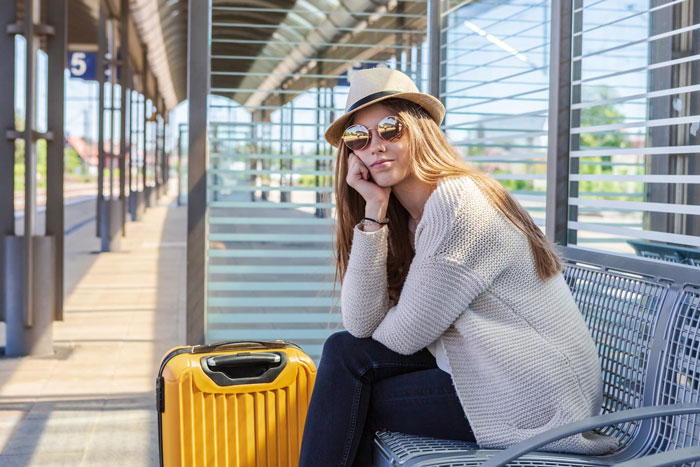 Young woman wearing sunglasses and a hat sitting with yellow suitcase at station, hinting roommate boyfriend vacation drama. Young woman wearing sunglasses and a hat sitting with yellow suitcase at station, hinting roommate boyfriend vacation drama.