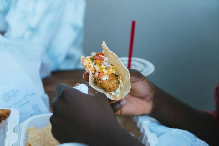 Hand holding a fried chicken taco with toppings, illustrating things normal in America but offensive elsewhere.
