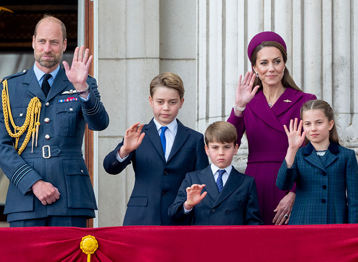 Royal family with children on balcony waving to crowd during formal event