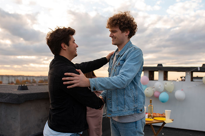 Two young men embracing on a rooftop, illustrating a moment related to grief and superhero interests.