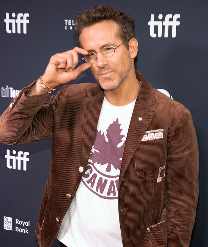 Ryan Reynolds at a film festival event, wearing glasses and a brown jacket posing for photos. Ryan Reynolds at a film festival event, wearing glasses and a brown jacket posing for photos.