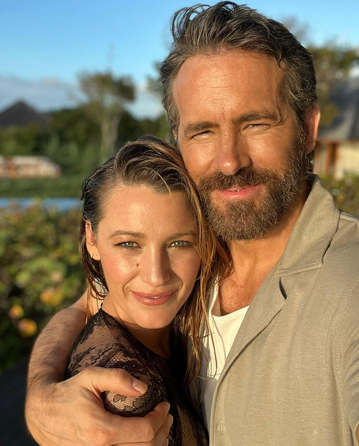 Ryan Reynolds smiling outside with a woman, with natural lighting highlighting their faces in a close embrace.