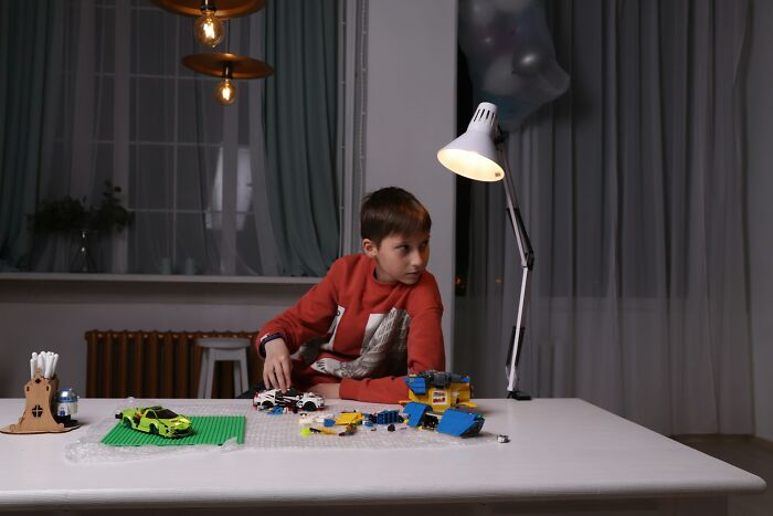 Boy at table assembling toy cars under lamp at night, suggests creepiest displays of intelligence